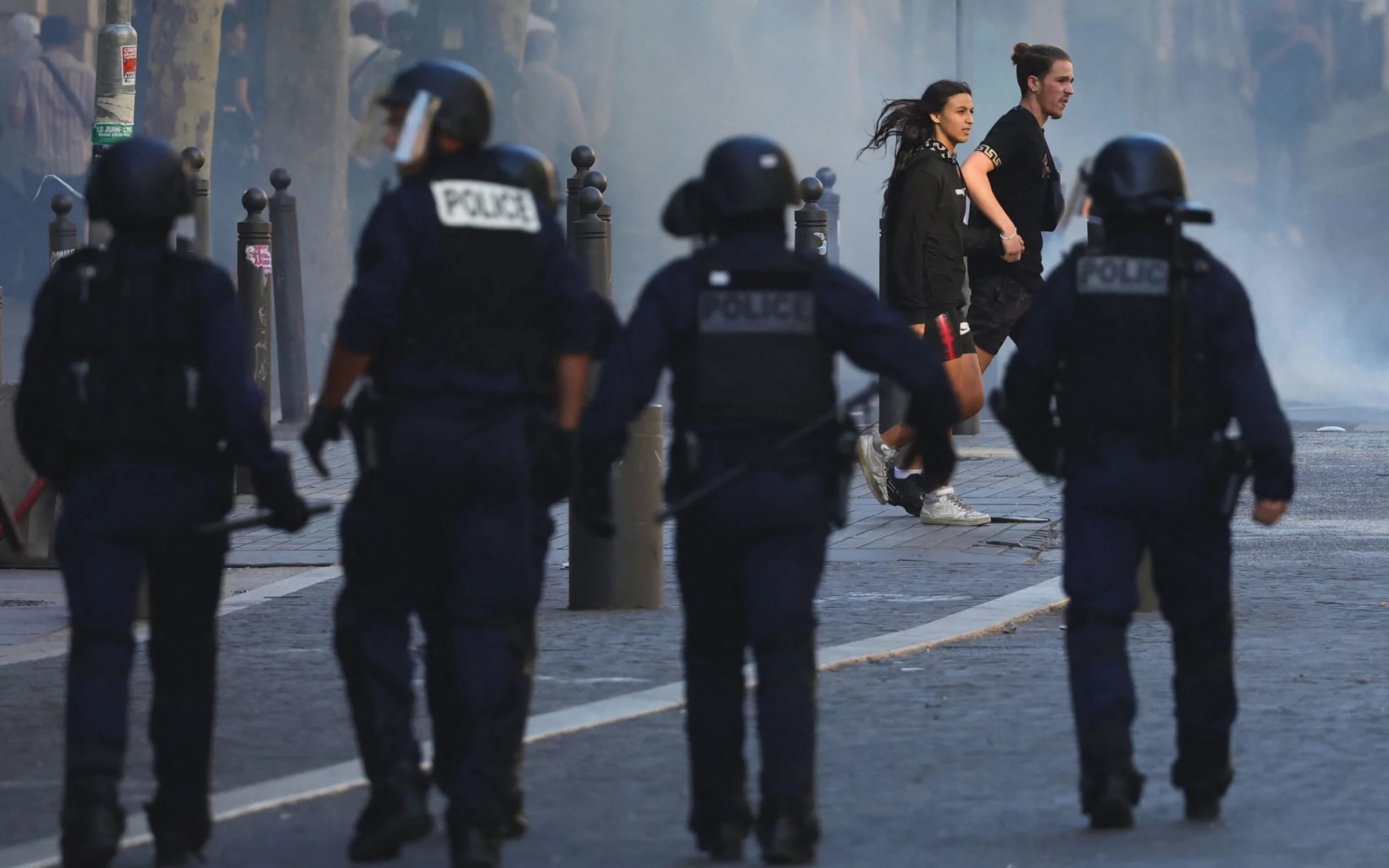 A man and a woman cross the street as police officers move in on protesters