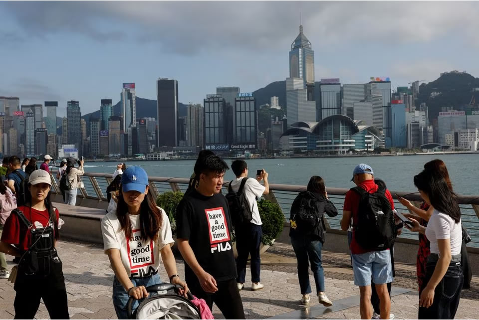 Mainland Chinese tourists walk in front of the skyline of buildings at Tsim Sha Tsui, in Hong Kong, China May 2, 2023